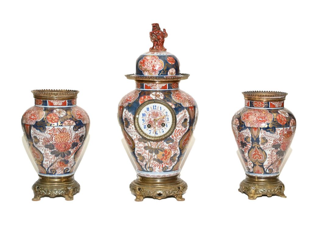 Antiquaire et brocanteur à Paris Un ensemble d'horloges de cheminée Trésor d'asie antique comprenant une horloge centrale et deux vases assortis. Ornée de motifs floraux complexes rouges, bleus et dorés, l'horloge centrale présente des détails en métal ornés et un dessus décoratif. Les vases et l'horloge reposent sur des bases élaborées en laiton.