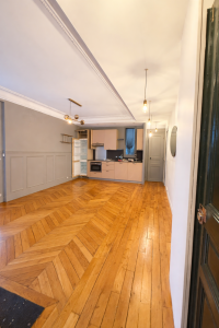 Pièce vide après débarras de succession avec parquet ancien et cuisine ouverte.