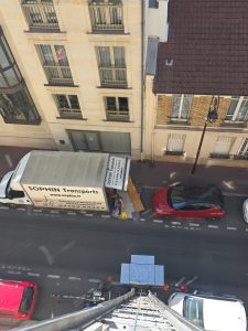Camion de déménagement stationné dans une rue de Paris avec monte-meubles déployé devant un immeuble.